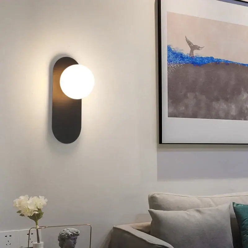 Modern black decorbites led glass ball wall sconce with oval backplate and glowing white spherical bulb for bedroom living room