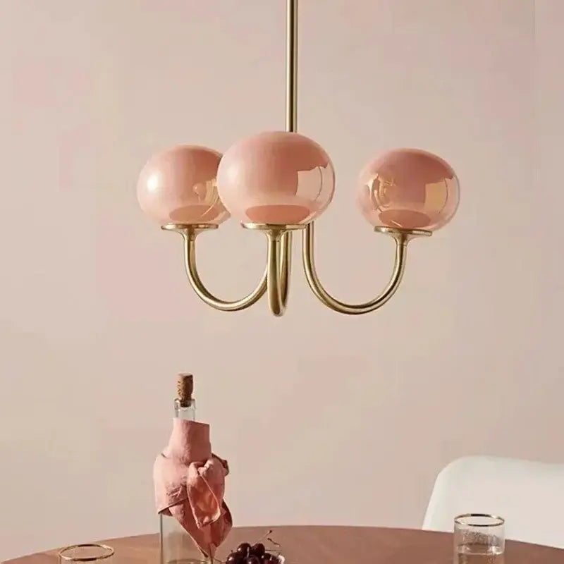 A delicate three-light decorbites led glass chandelier with rose-tinted glass balls and polished brass frame for home decor