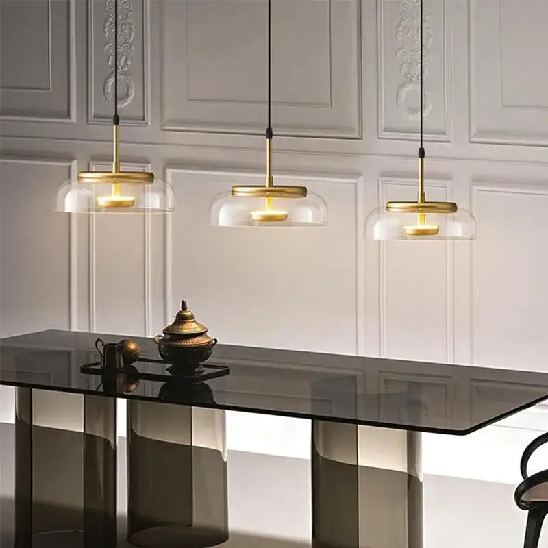 Three elegant gold-toned decorbites led glass bowl pendant lights hang above a sleek black table in a modern setting