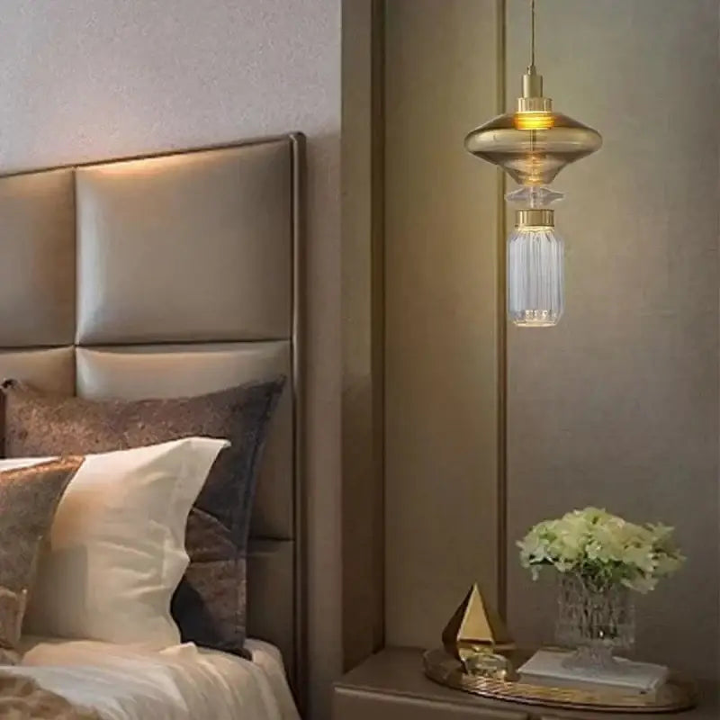 A modern gold-toned decorbites led glass chandelier with clear amber glass and adjustable wire above a bedside table