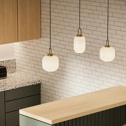 Three white ribbed glass pendant lights with brass accents hang from black cords in decorbites led glass chandelier