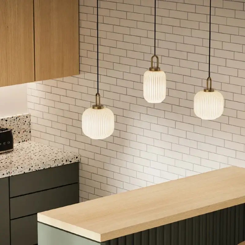 Three white ribbed glass pendant lights with brass accents hang from black cords in decorbites led glass chandelier