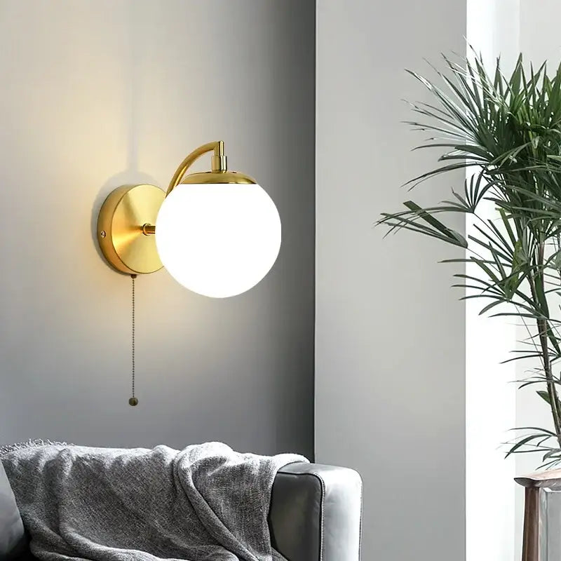 Gold-toned decorbites led glass iron wall light with spherical frosted glass shade and curved arm for corridor or bedroom