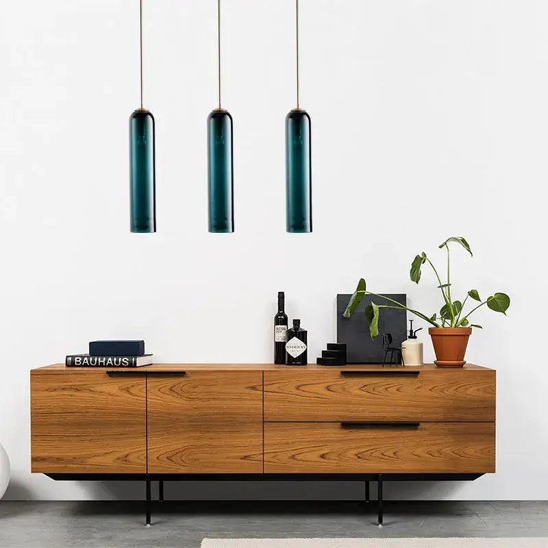 Three sleek dark teal cylindrical decorbites led glass pendant lights hang above a wooden sideboard for kitchen decor