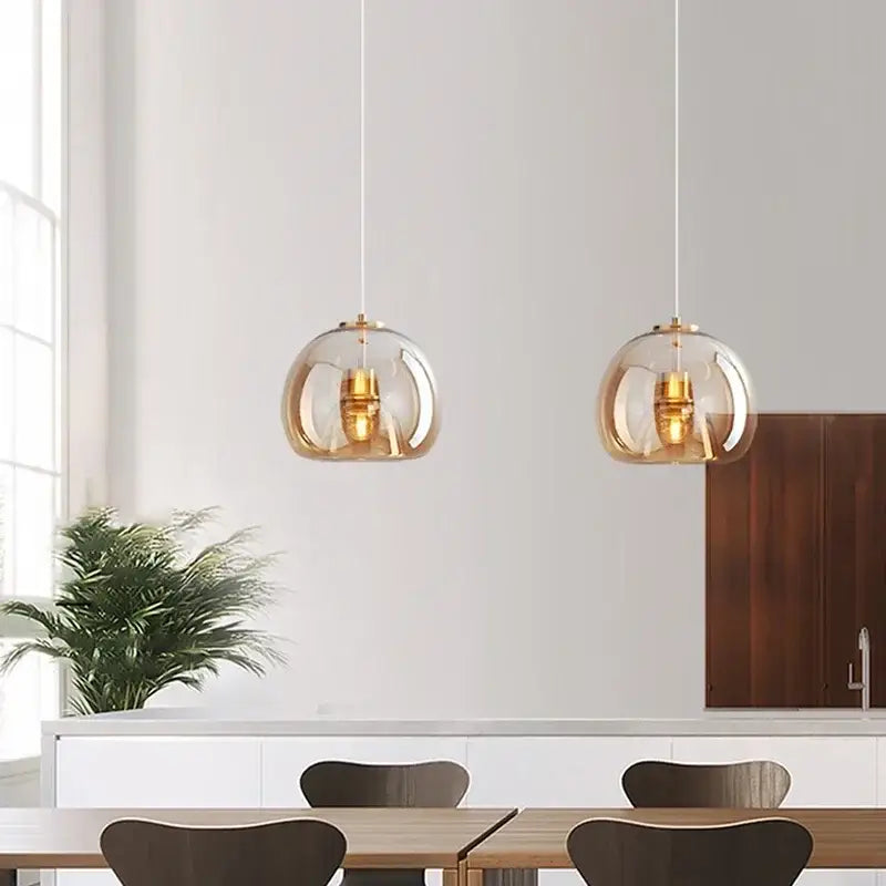 Two amber-tinted glass globe pendant lights with brass hardware hang from white cords in decorbites led glass pendant light