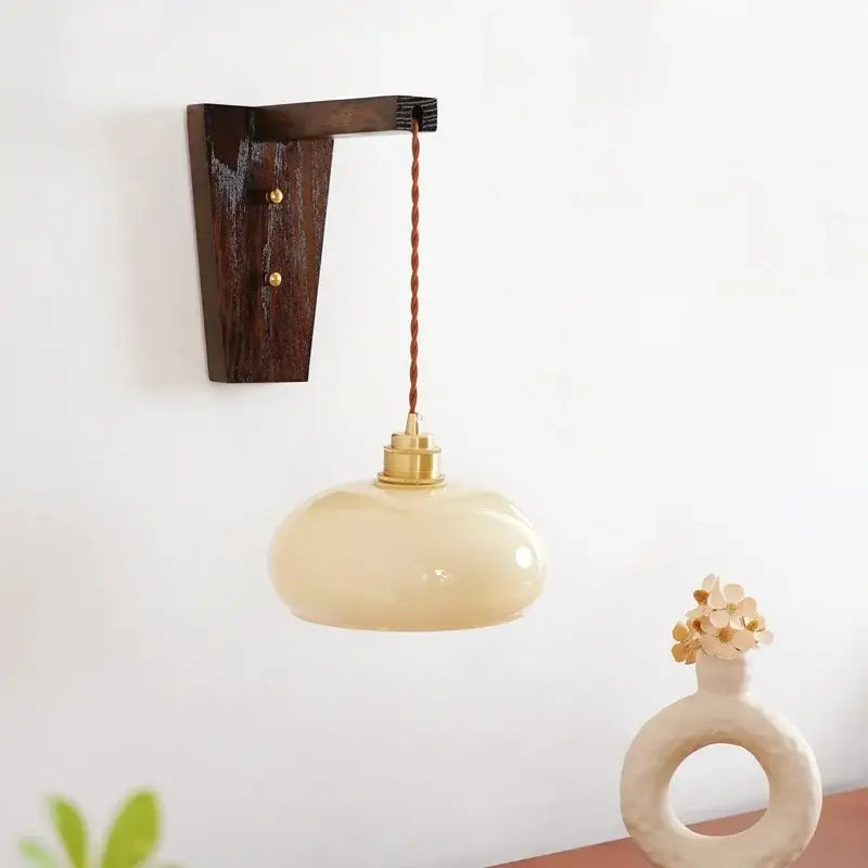 Cream-colored led glass sconce wall lamp with brass fixture and twisted cord mounted on dark wood decorbites led glass bracket