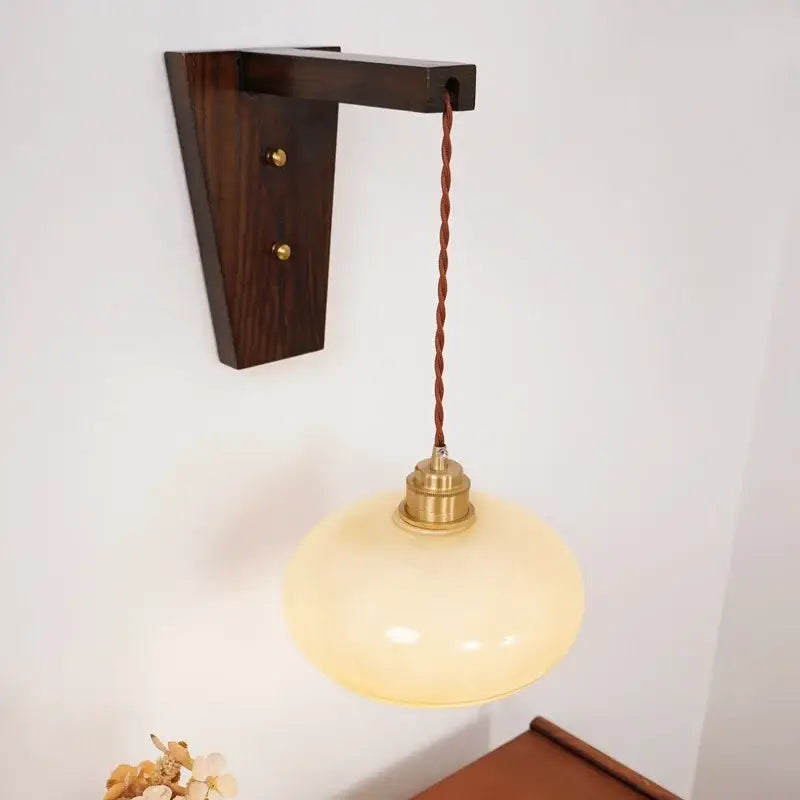 Warm cream-colored led glass sconce wall lamp by decorbites with brass fixture and twisted brown cord on dark wood bracket