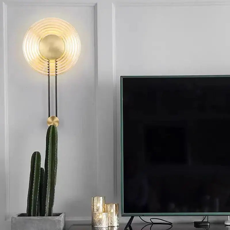 Gold-toned DecorBites™ LED glass wall lamp with concentric ridges and a hanging spherical accent for elegant lighting