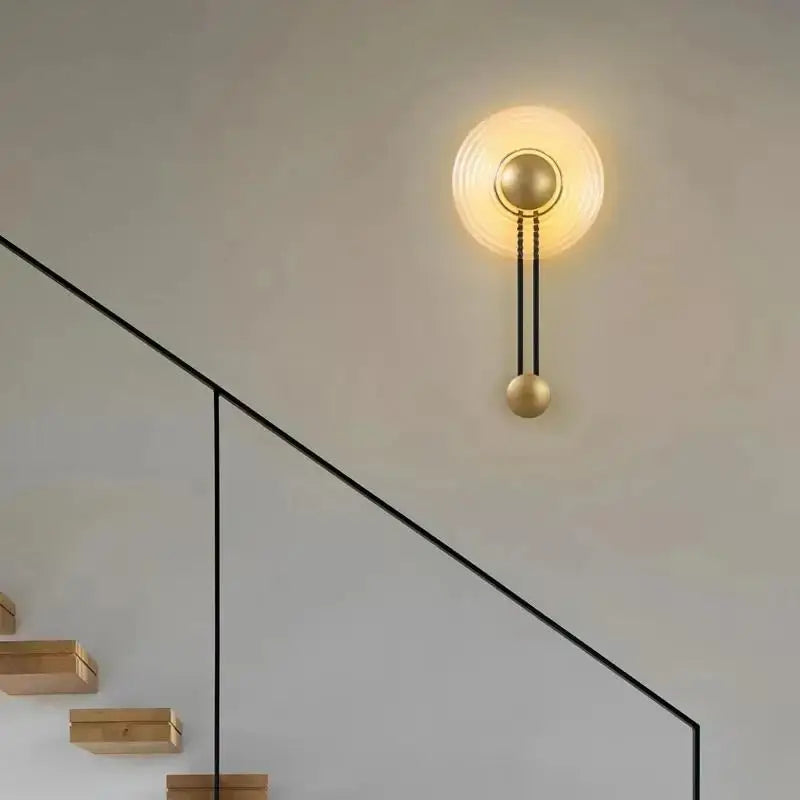 Gold-toned decorbites led glass wall lamp with circular ribbed glass shade and brass accents connected by black chains