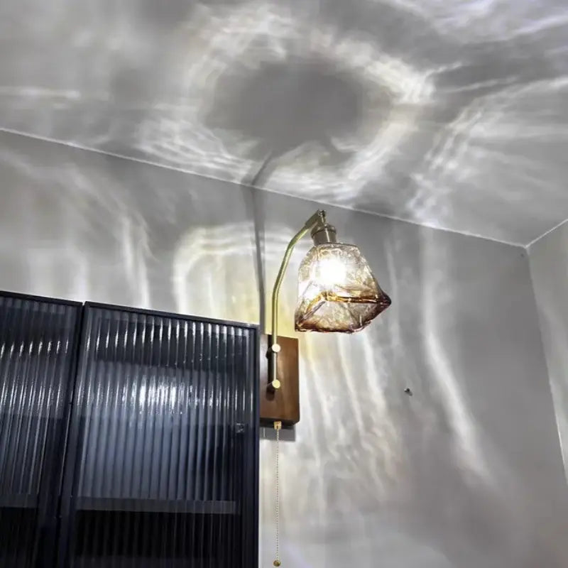 DecorBites™ LED brass-finished wall lamp with amber glass shade casting light patterns for living room and bedroom