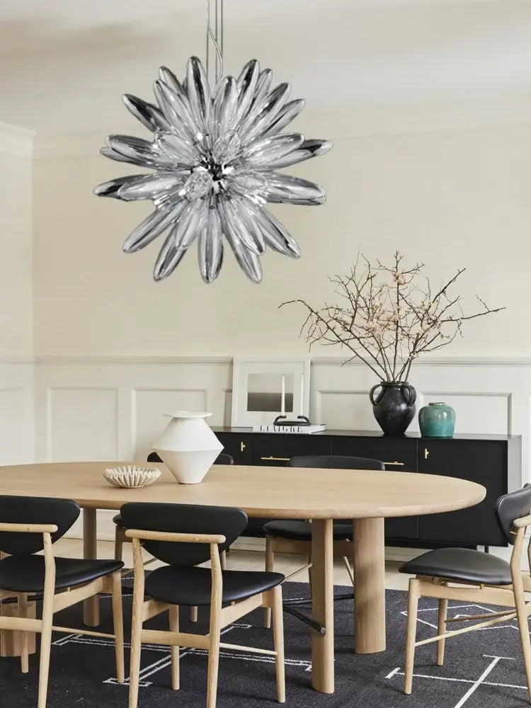 A modern silver-toned glass decorbites led globe chandelier with starburst design hangs above the dining table