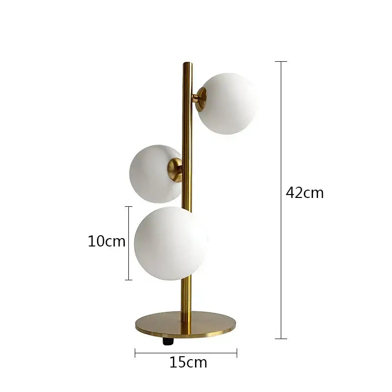 Modern brass table lamp with three milk white glass frosted spherical shades in a vertical cluster by DecorBites