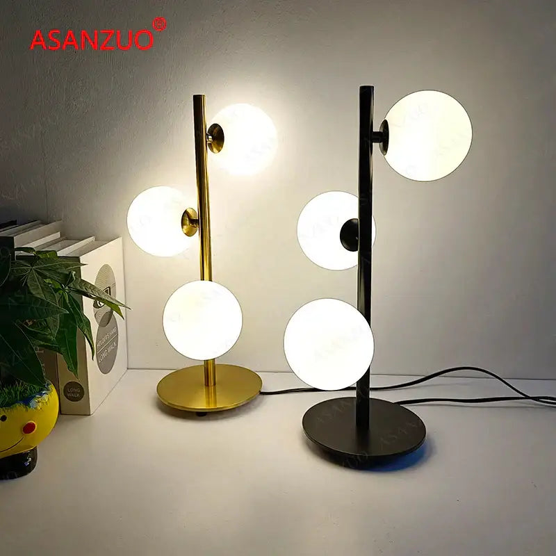 DecorBites™ LED gold table lamp with sleek metallic stand and milk white glass spherical white glass lampshade next to black lamp