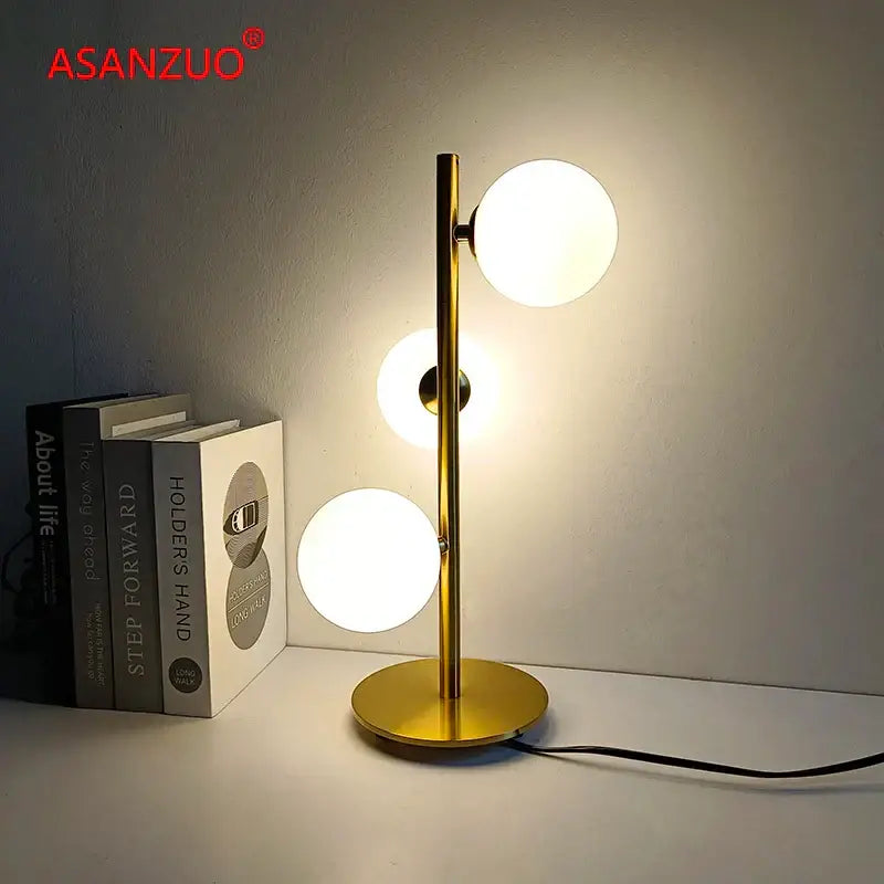 Gold-toned DecorBites™ LED table lamp with three milk white glass globes on a sleek metallic stand and white glass lampshade