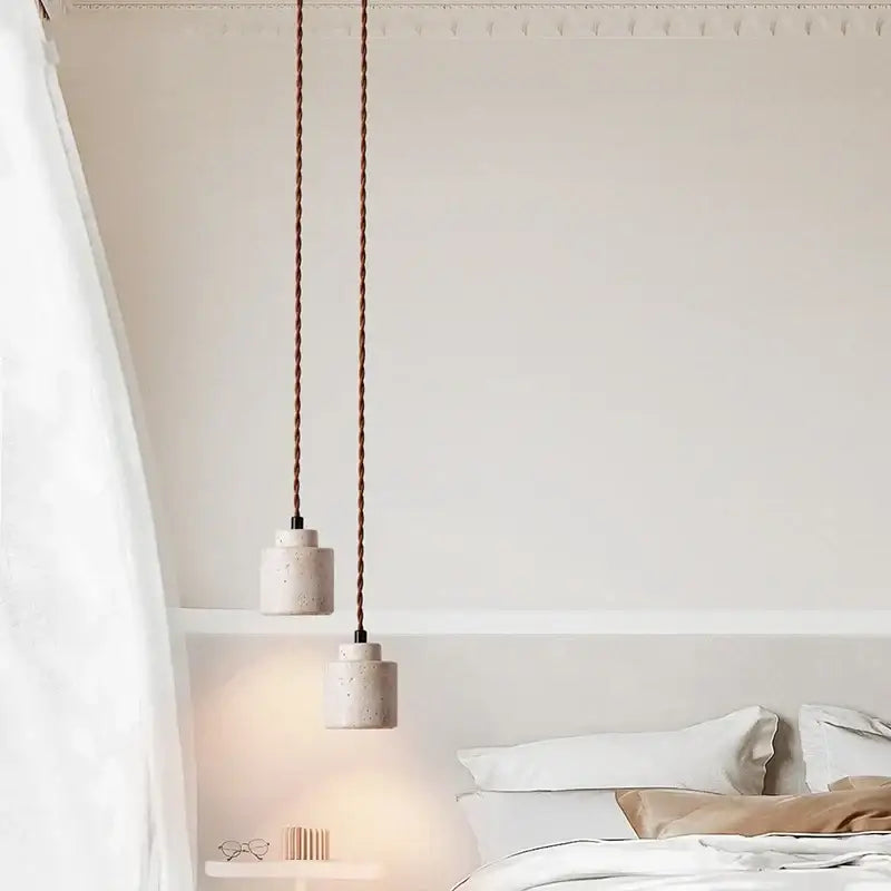 Two minimalist decorbites led hanging pendant lights with yellow travertine textured concrete shades above a bed