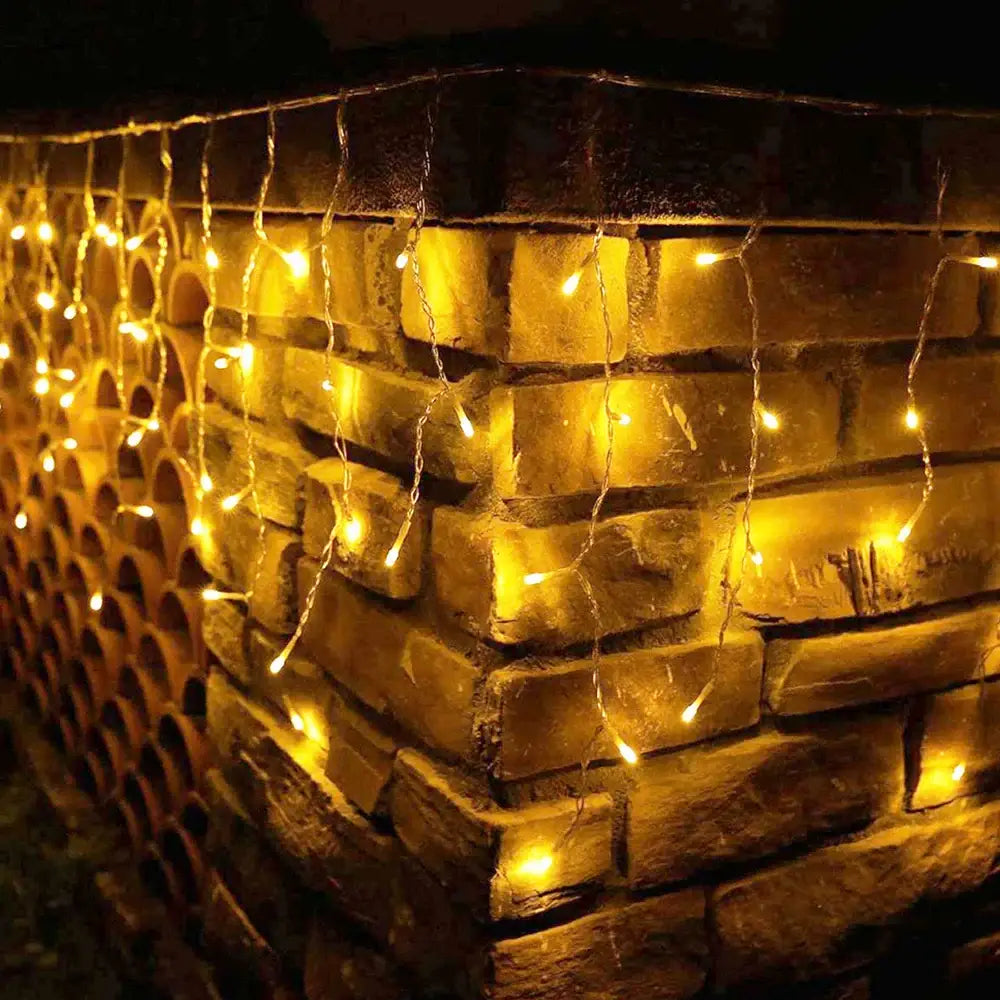DecorBites™ warm yellow led icicle string lights hanging in cascading strands on textured brick wall for outdoor decor