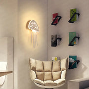 A white illuminated perforated led jellyfish wall lamp with dangling tentacles by decorbites for modern indoor decor