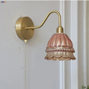 A delicate pink glass lampshade with a fluted design hangs from a brass arm in the decorbites led jellyfish wall lamp