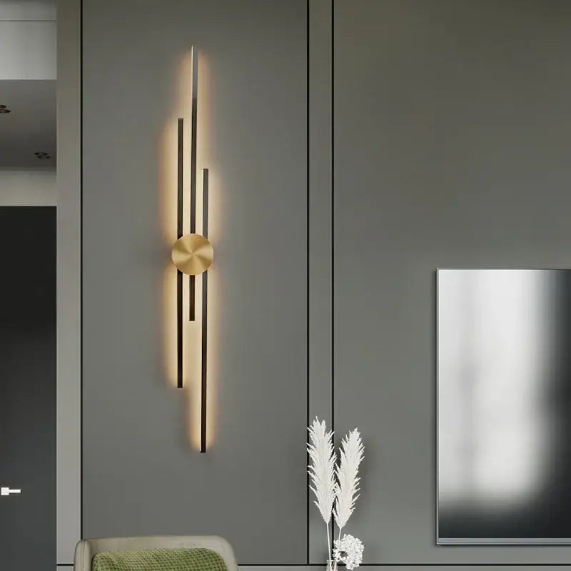 Modern gold-toned decorbites led long wall lamp with vertical rods and circular base emitting warm light on dark cabinetry