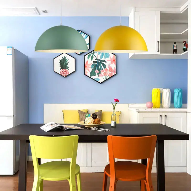 Two dome-shaped pendant lights in matte green and mustard yellow from DecorBites led Macaron pendant collection above table