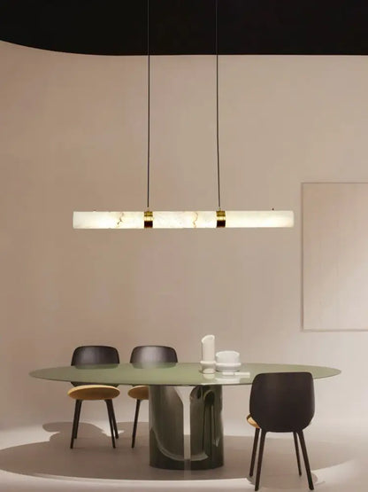 A sleek rectangular led marble hanging lamp in white alabaster with gold accents hanging above a dining table
