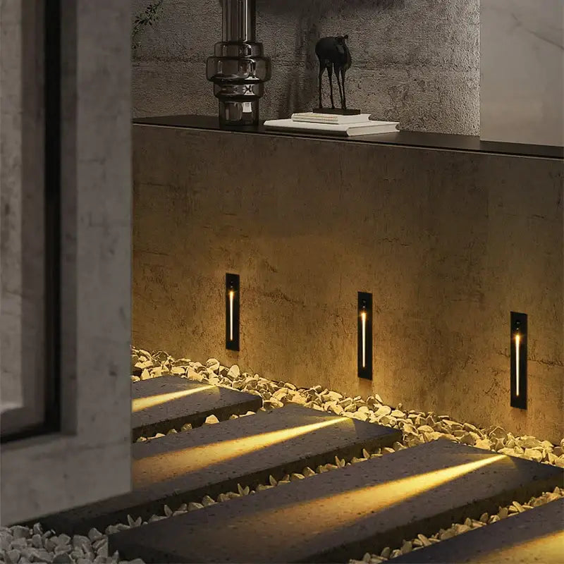 Three sleek black decorbites led motion sensor wall lamps illuminate a stone pathway with warm golden light