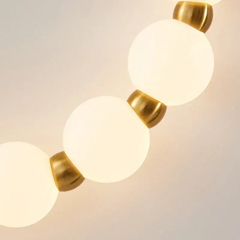 A decorbites led necklace wall light featuring frosted white glass bulbs with polished brass accents for home lighting