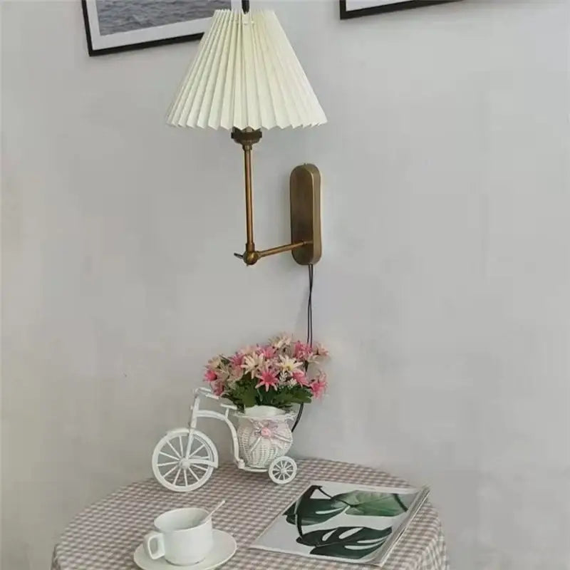 A cream-colored pleated lampshade mounted on a brass wall sconce for decorbites led origami wall lamp
