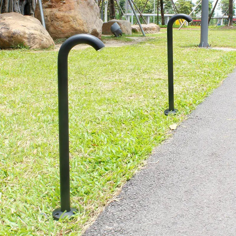 Black metal bike rack posts with curved tops in grassy park beside decorbites led outdoor aluminum bollard light