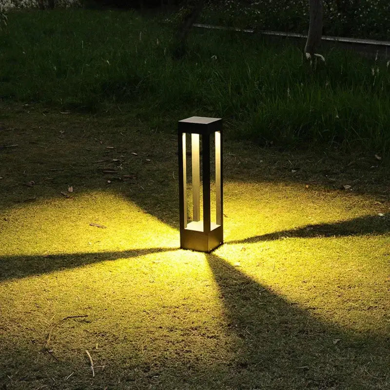 Black rectangular decorbites led outdoor lawn light with vertical glass panels emitting warm yellow glow for garden use