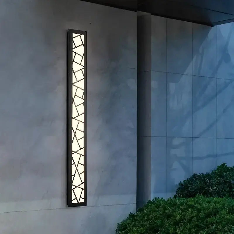 Modern black-framed decorbites™ outdoor wall lamp with geometric glass panels emitting a warm ambient glow