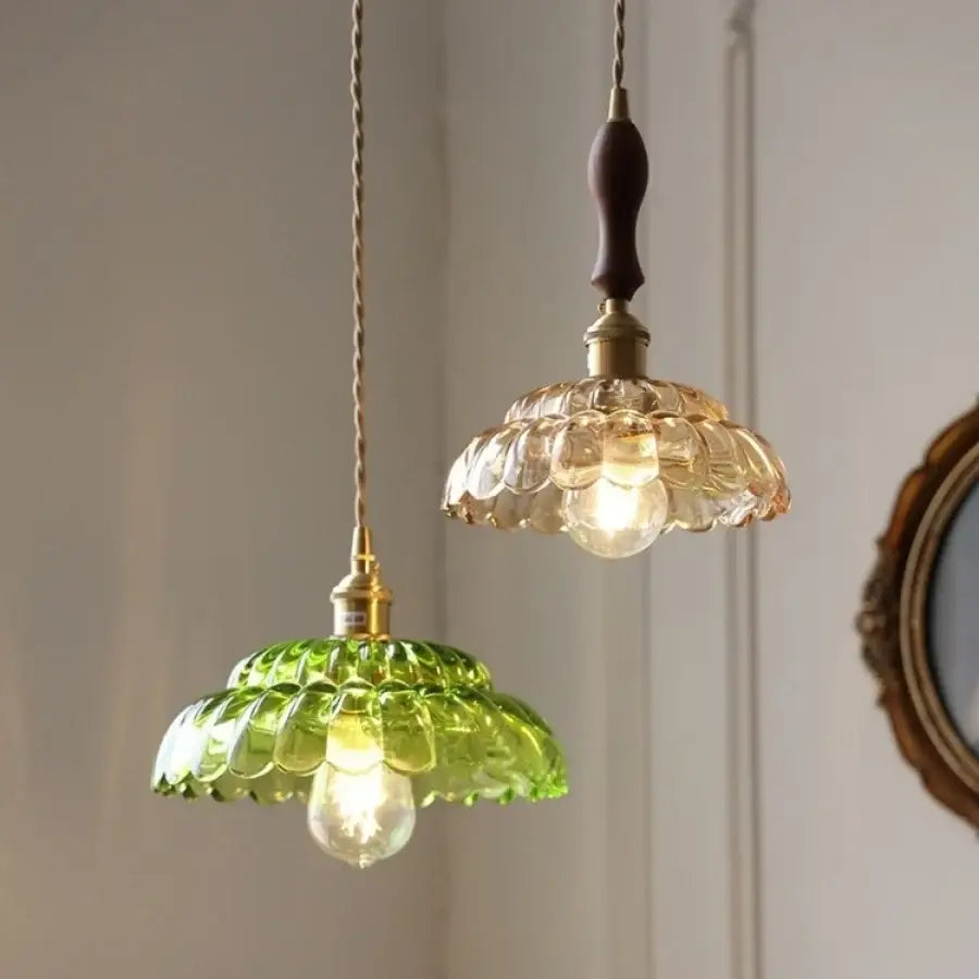 Two decorbites led pendant lamps with emerald green and amber scalloped glass shades hang from twisted copper cords