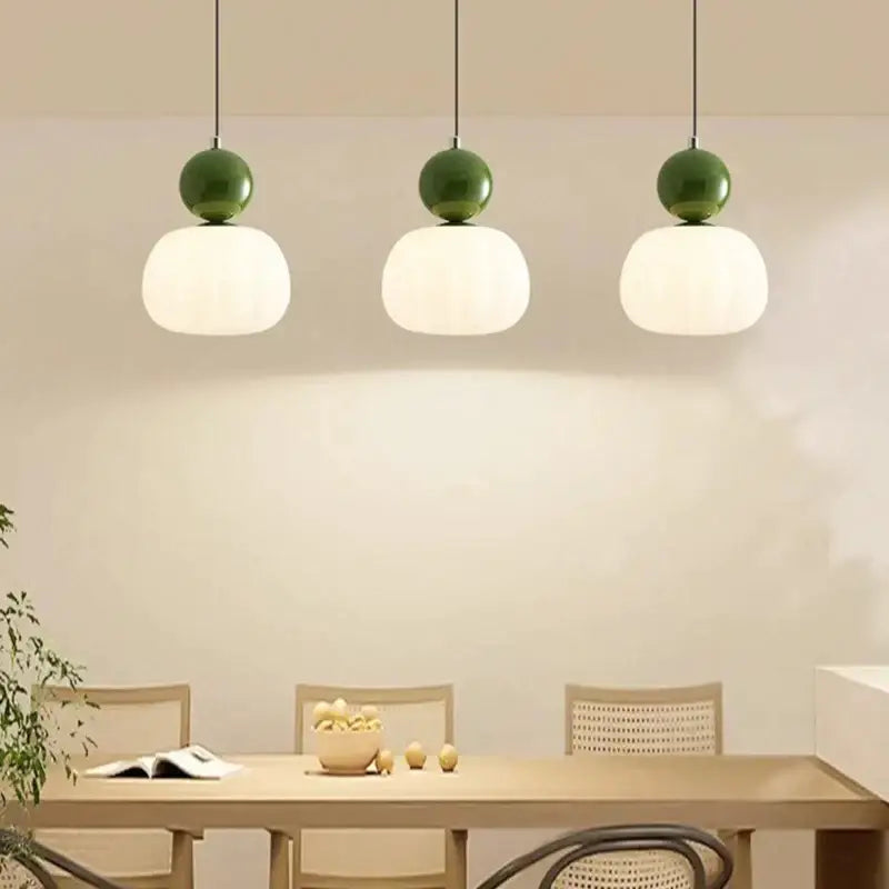 Three matte green led pendant lamps with frosted white globe shades hang above a dining table by decorbites