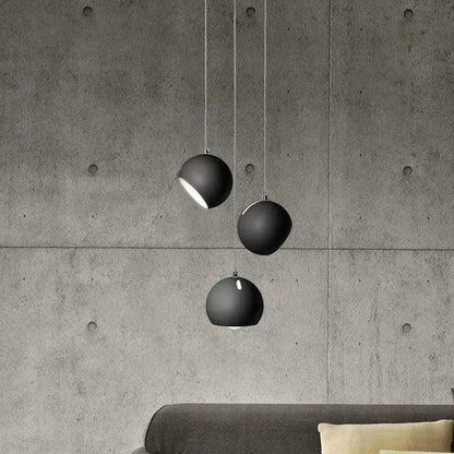 Three matte black spherical decorbites led pendant lights hang from cords against a concrete wall
