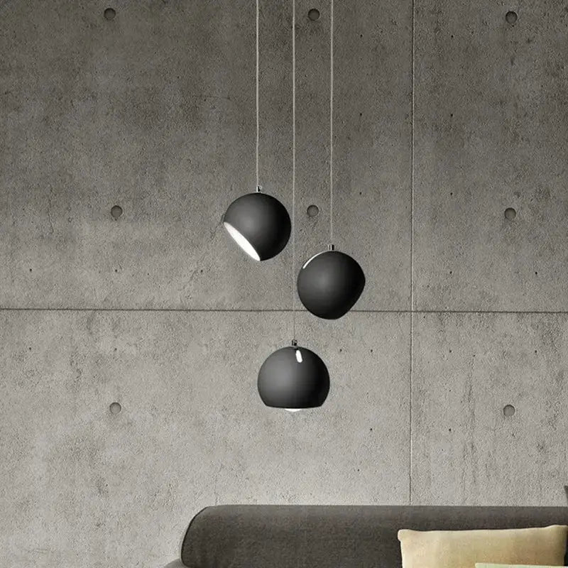 Three matte black spherical decorbites led pendant lights hang from cords against a concrete wall