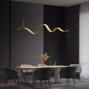 Golden wave-shaped DecorBites LED pendant light with sleek metallic finish hangs above dining table for modern decor
