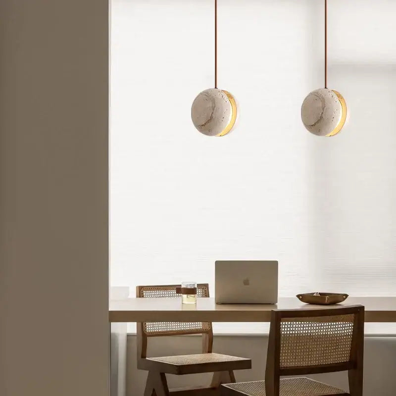 Two decorbites led pendant lights with yellow travertine marble shades and brass accents hang above a dining table