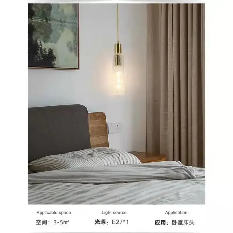 Gold-toned decorbites led pendant light with cylindrical glass shade and exposed filament bulb hanging above bed