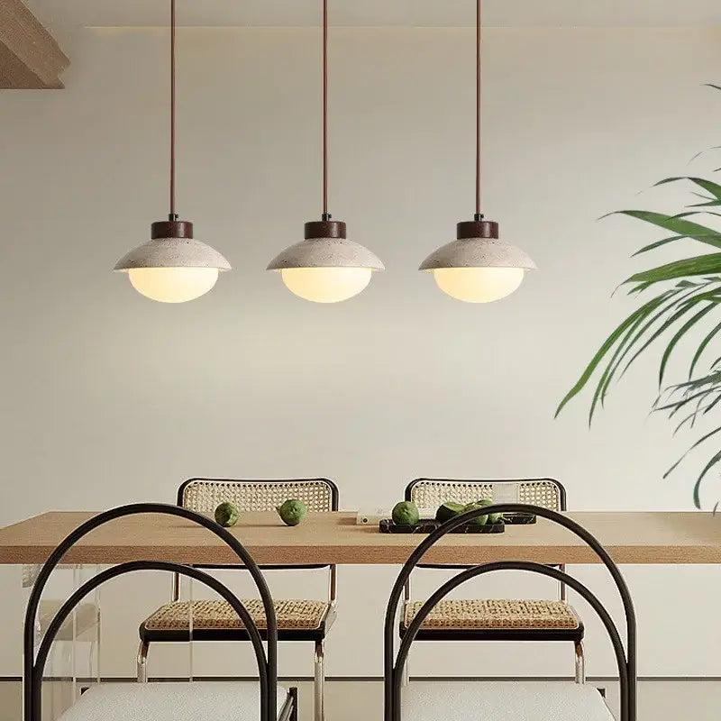 Three decorbites led pendant lights with yellow travertine wood and concrete shades hang above a dining table
