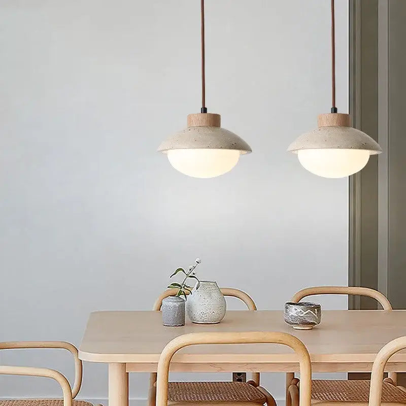 Two beige ceramic decorbites led pendant lights with yellow travertine wood accents hang above a wooden dining table