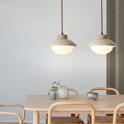 Two beige ceramic decorbites led pendant lights with yellow travertine wood accents hang above a wooden dining table