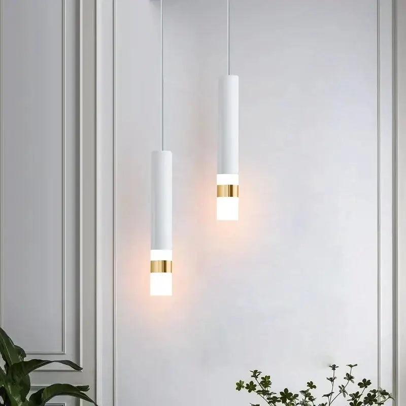 Two minimalist white matte cylindrical pendant lights with gold bands emitting warm glow decorbites led pendant light