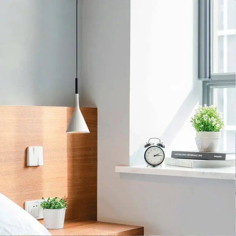White conical decorbites led pendant light with black cord hanging above wooden bedside table for modern interiors