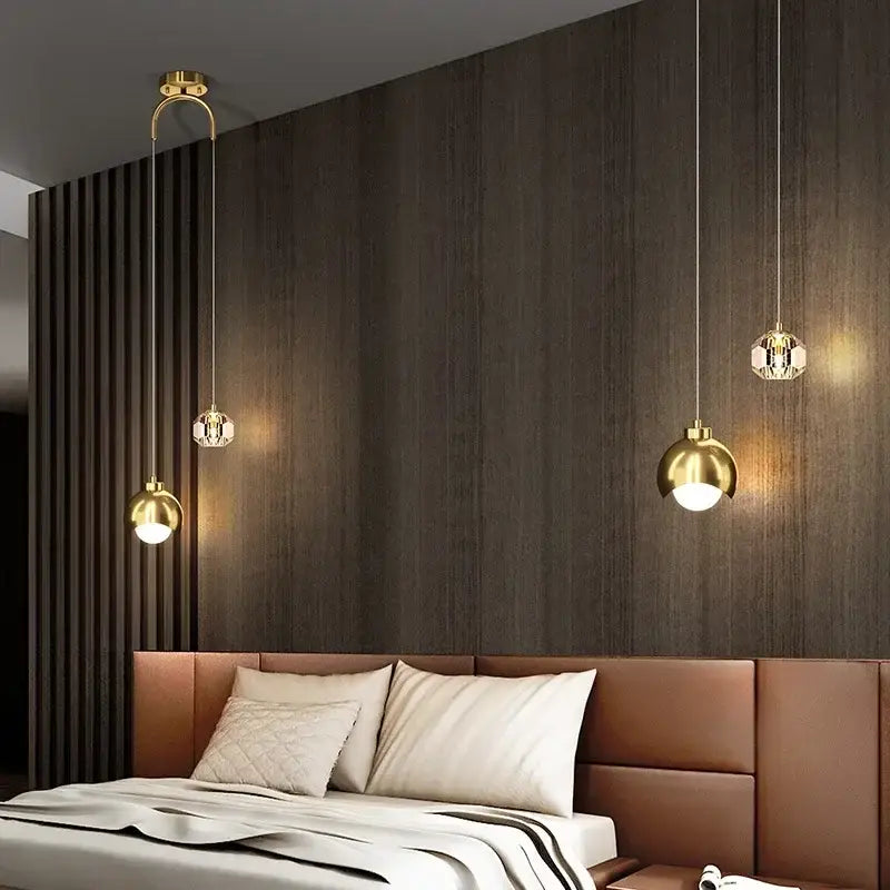 Three elegant gold-toned DecorBites LED pendant lights with crystal shades hang above a bed for luxury decor