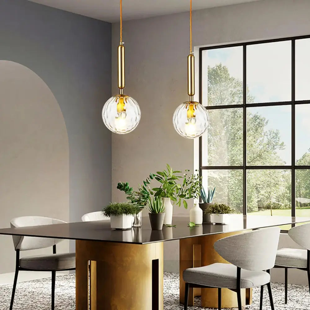 Two elegant gold-finished DecorBites LED pendant lights with clear faceted glass globes hang above a dining table