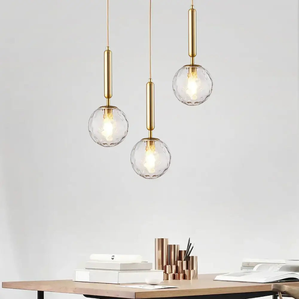 Three elegant gold-finished decorbites led pendant lights with faceted glass globes hang above a wooden desk