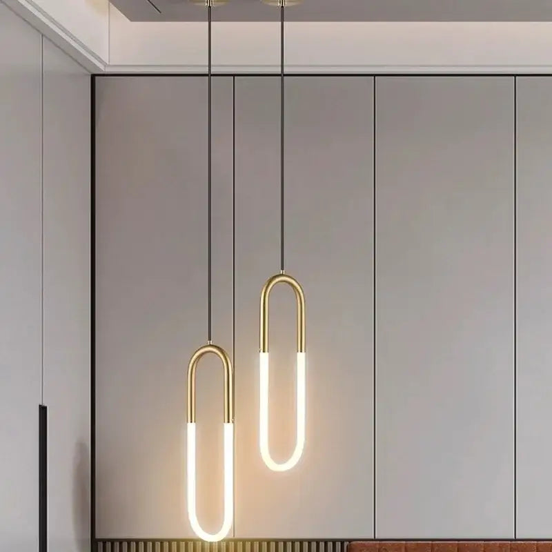 Two decorbites led pendant lights with gold metal frames and white led tubes hang against a minimalist gray wall