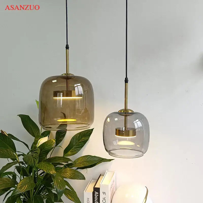 Two modern decorbites led pendant lights with smoked and clear glass shades, brass accents, and black cords for home decor