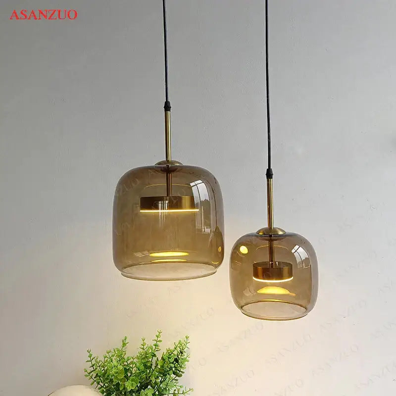 Two amber-tinted glass decorbites led pendant lights with brass accents hang from black cords for modern decor