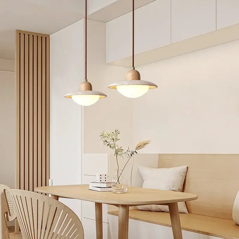Two decorbites led pendant lights with yellow travertine wood caps and textured concrete shades hang with warm glow